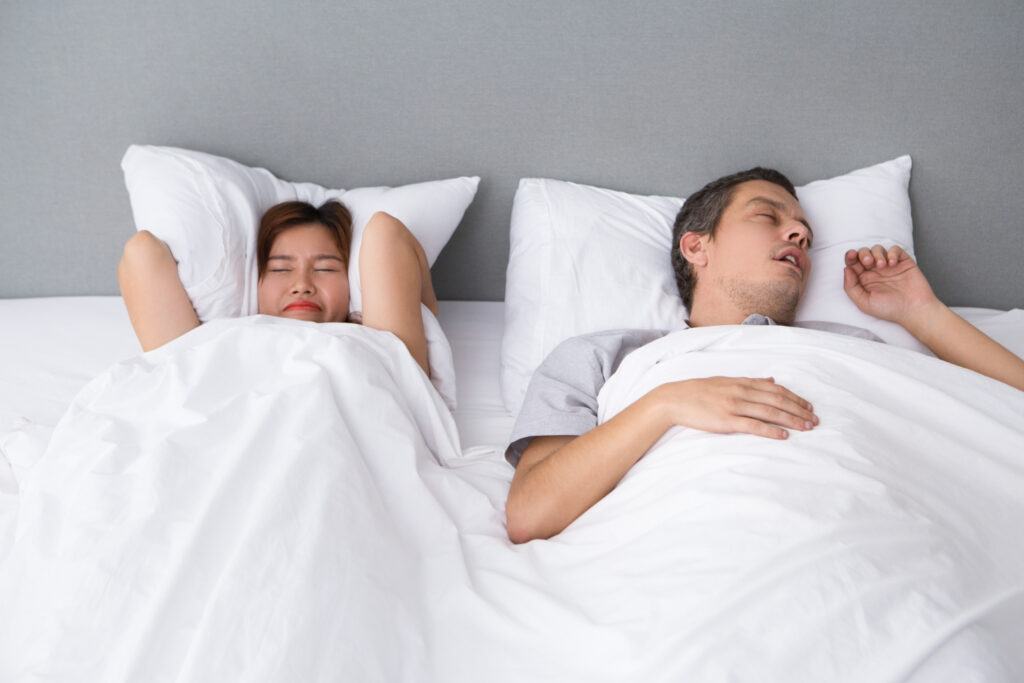 Gegen Schnarchen gibt es in der Schlafmedizin gute Erfolge. Ein paar liegt zusammen im Bett und die Frau drückt sich das Kissen auf die Ohren.