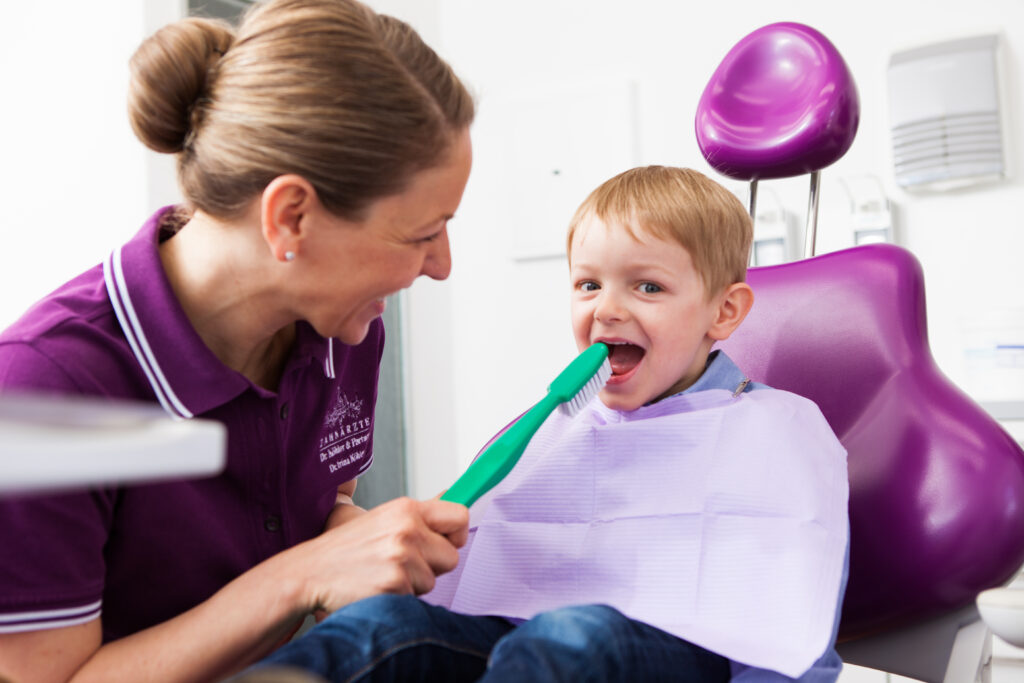 Dr. Irina Köhler hält einem kleinen Jungen eine große Zahnbürste vor den Mund.